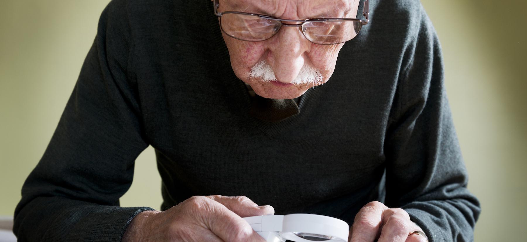 Image of an older male looking at a newspaper using a magnifying glass